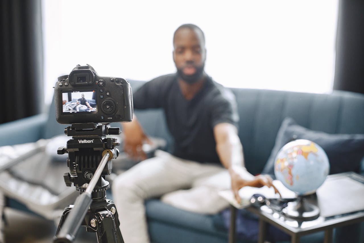 A content creator adjusts a DSLR camera on a tripod for video blogging indoors.